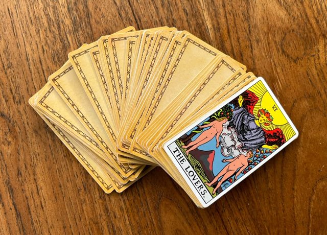 A fanned tarot deck on a wooden table, with The Lovers card turned face up